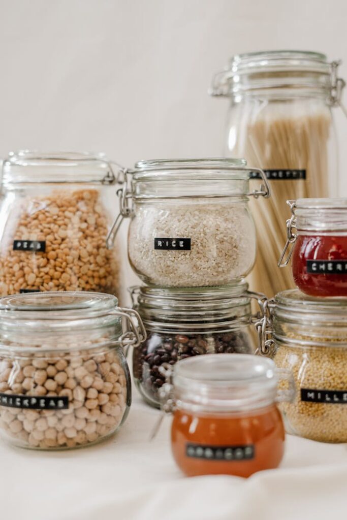 Glass jars filled with diverse kitchen ingredients like rice and chickpeas on a white background.